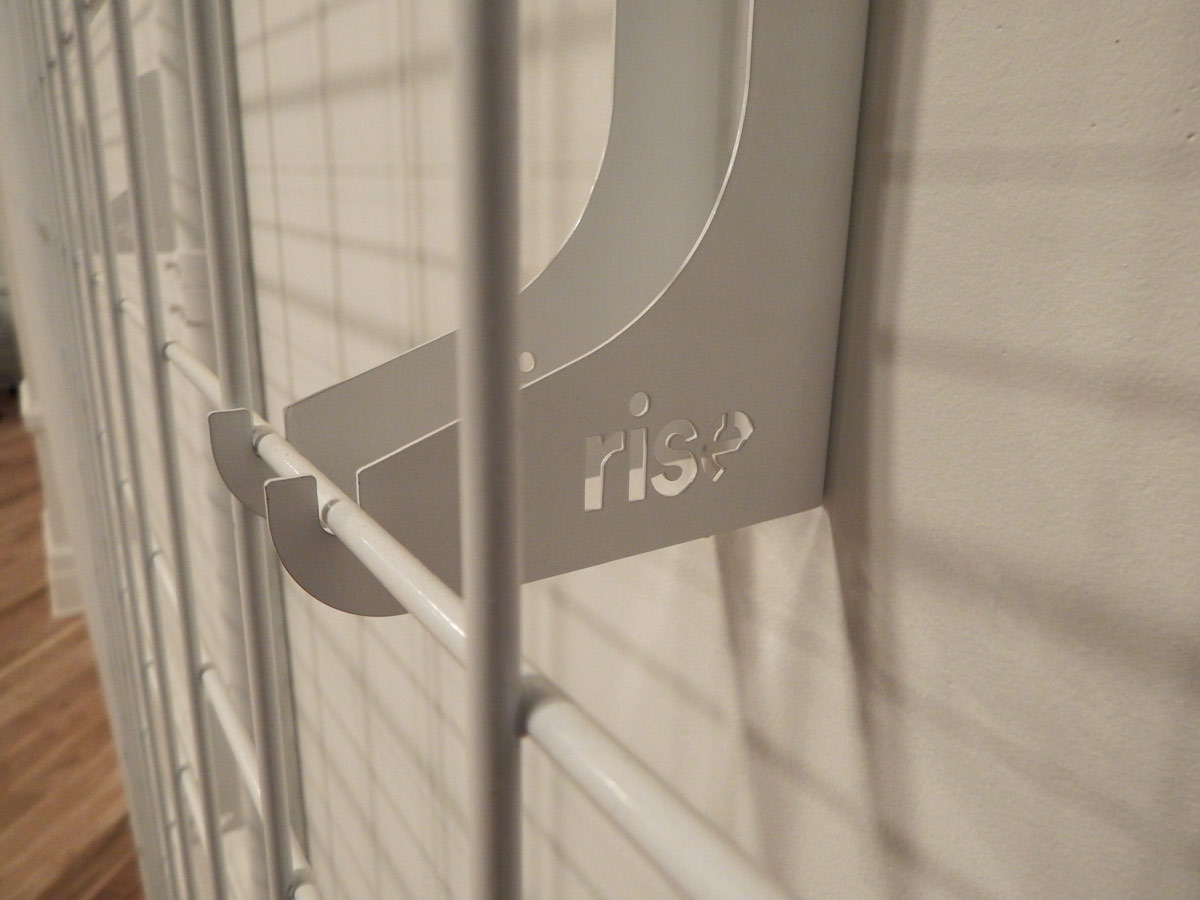 White metal grid with a hook and the word "rise" cut into it.