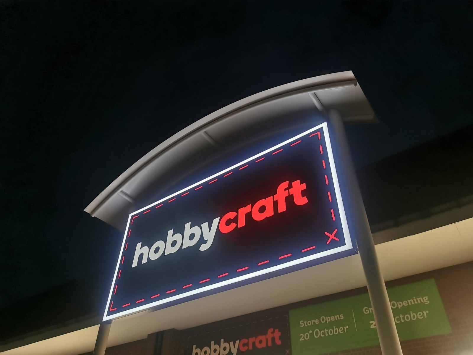 Illuminated "hobbycraft" sign with a curved roof against a dark night sky.