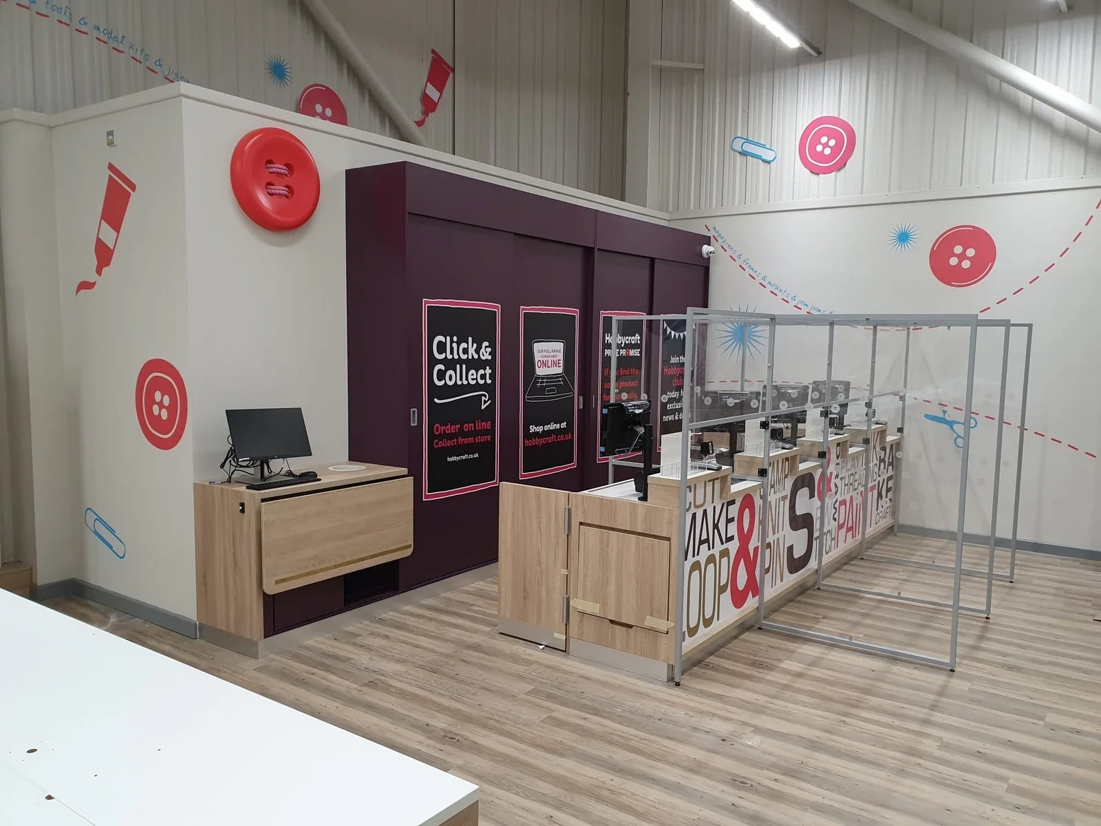 Click and collect counter with a computer, signage, and decorative button graphics on walls.