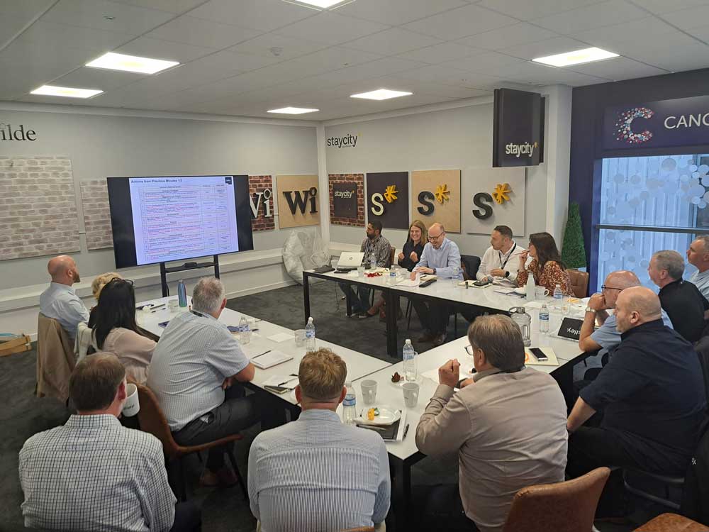A group of people seated around a conference table watching a presentation on a screen.