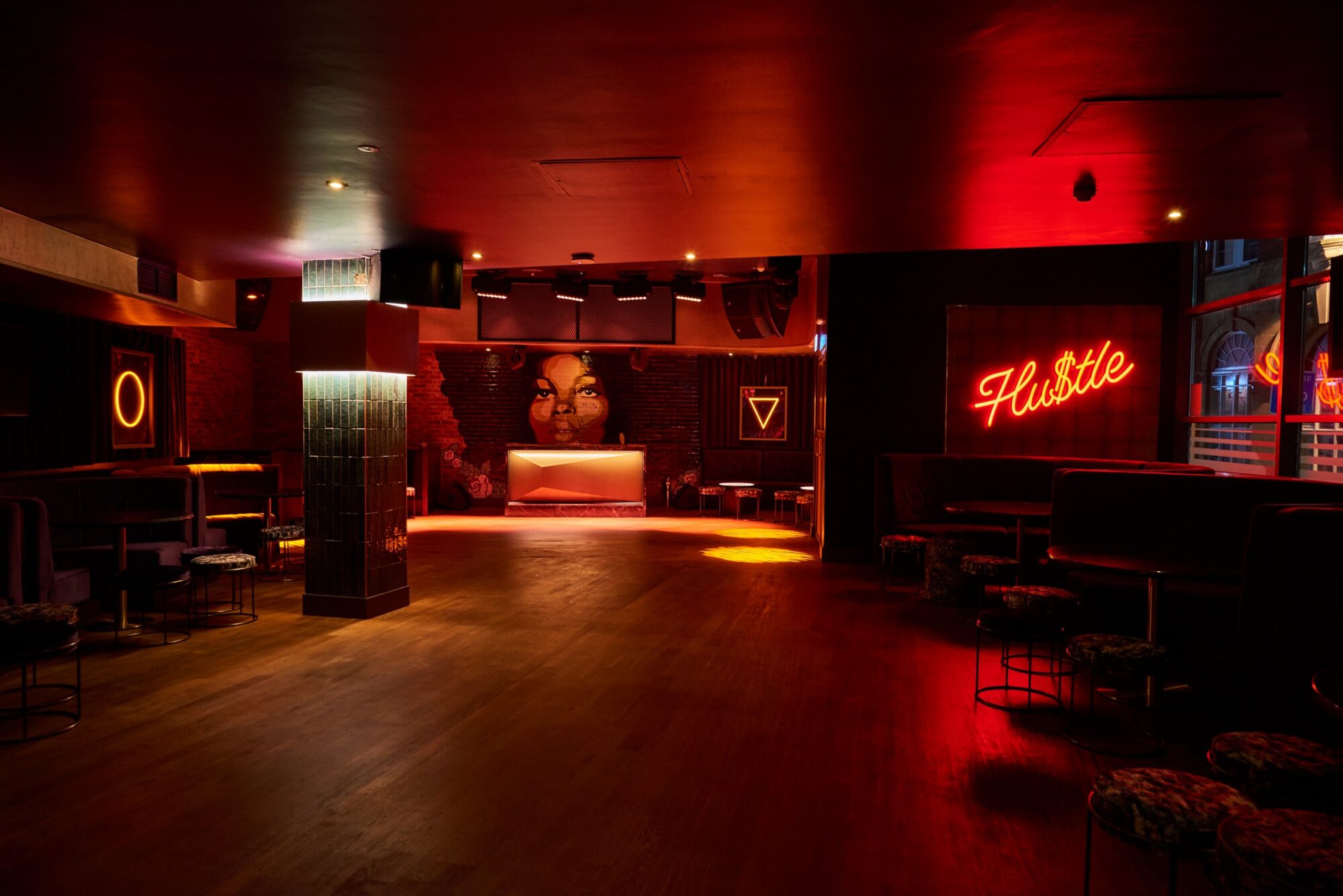 Dimly lit nightclub interior with red neon signs, bar area, and scattered seating.