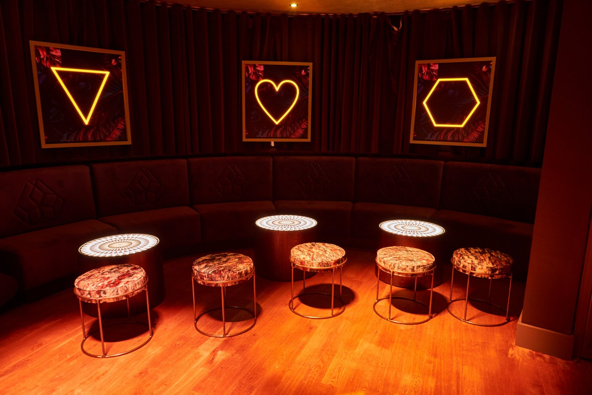 Dimly lit lounge with circular tables, patterned stools, and neon geometric shapes on the walls.
