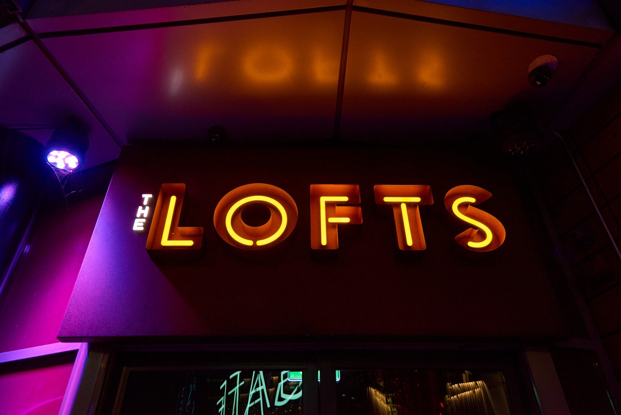 Illuminated sign reading "THE LOFTS" in bold, glowing letters against a dark background.