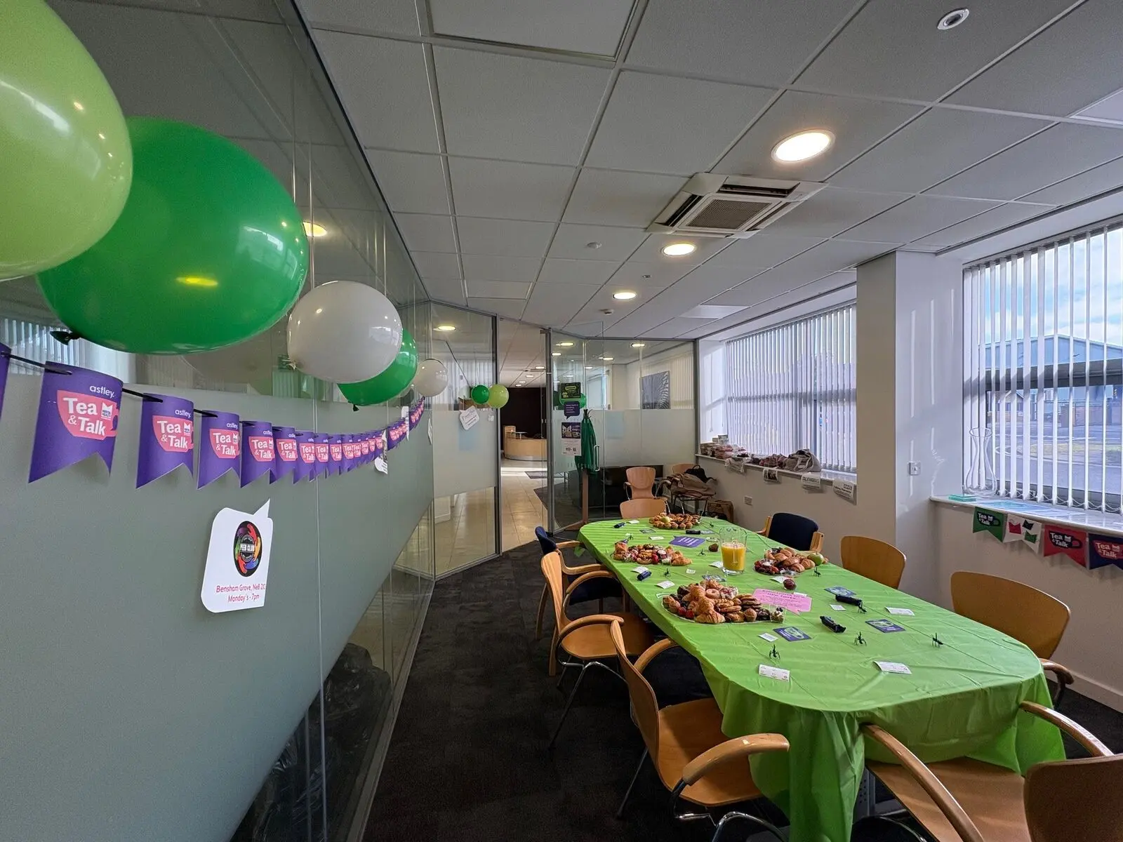 Office room decorated with green balloons and a table set for a party with snacks.