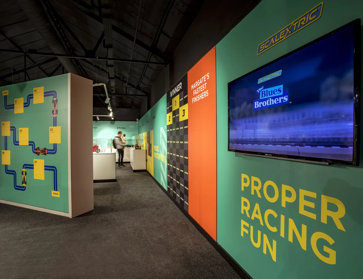 Exhibit room with colorful walls, a TV screen, and a person in the background.