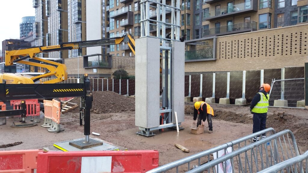 Structural steel totem being installed on site, lifted into position beside a completed base